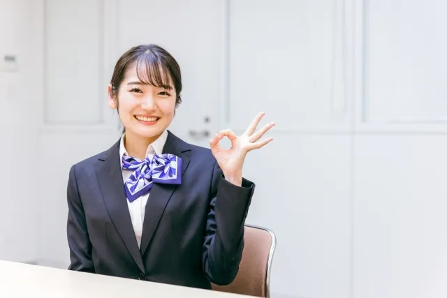 屋内イベントの受付業務を行う、手でOKサインを作る女性スタッフ
