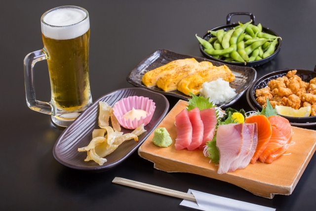 ビールとともに机に並ぶさまざまな居酒屋メニューのイメージ