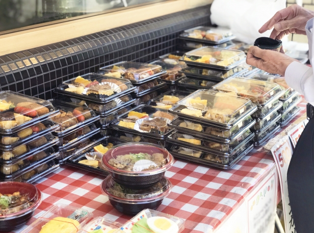 店に並ぶさまざまなお弁当とそれを吟味するお客様の手元のイメージ