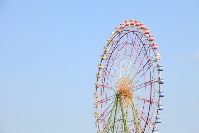 青空をバックに立つテーマパークの観覧車のイメージ