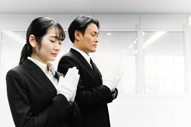 白手袋をつけて合掌するスーツ姿の男女スタッフ