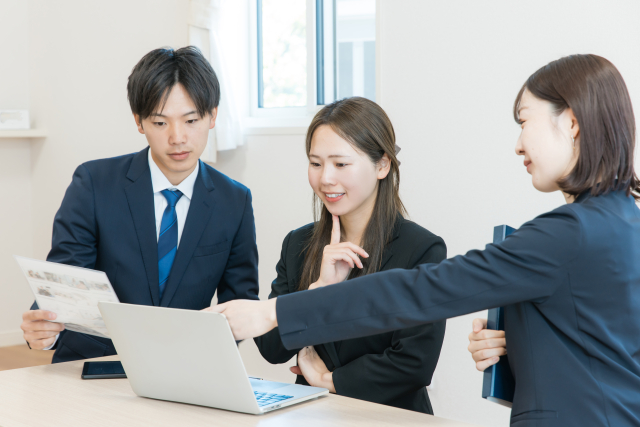 パソコンと紙の資料を比較している3人のスーツ姿の男女