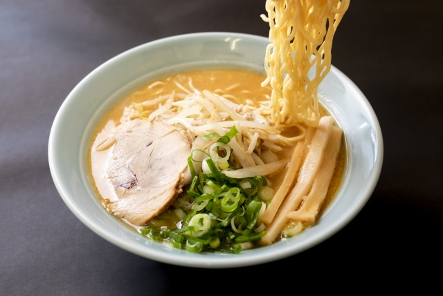 黒い背景に置かれた湯気を上げているラーメンのイメージ