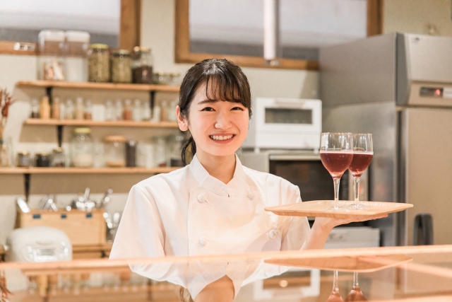 トレーにのった赤ワインを持つ飲食店の女性店員