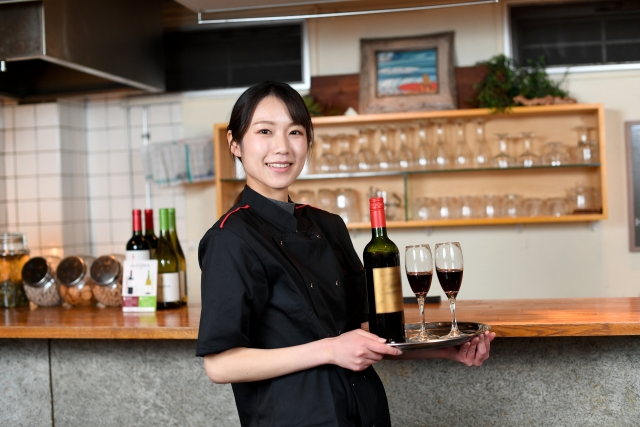 ワインとグラスをトレーで運ぶ女性店員