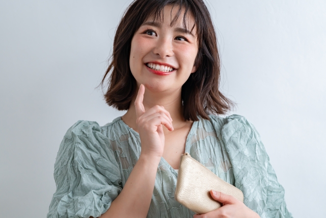 金色の財布を手に微笑みながら何かを考える女性