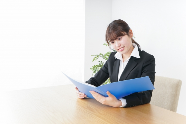 青いファイルの中身を確認するスーツ姿の女性