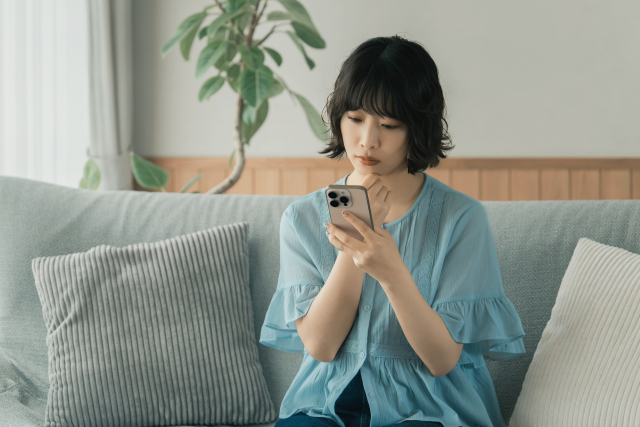 顎に手を当てて考え込みながらスマホを見つめている女性