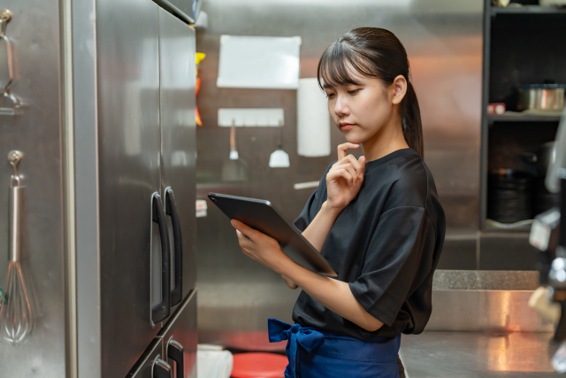 厨房にある冷蔵庫の前でタブレットをチェックする女性スタッフ