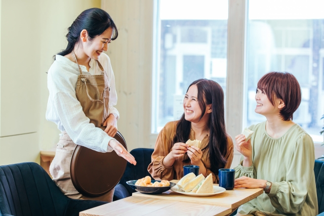カフェで女性客二人組に料理を提供する女性店員