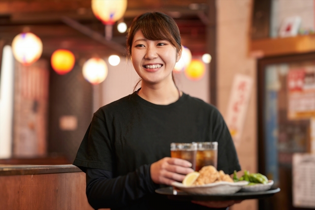 トレーで料理やドリンクを提供している飲食店の女性スタッフ