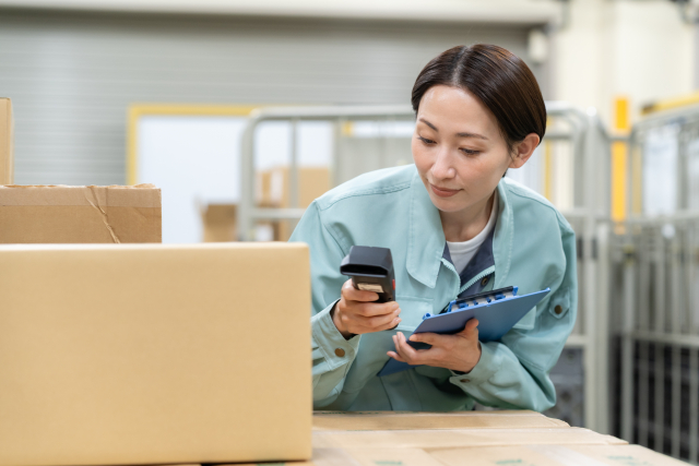 バーコードを確認しながら仕分け作業を行う作業着姿の女性スタッフ