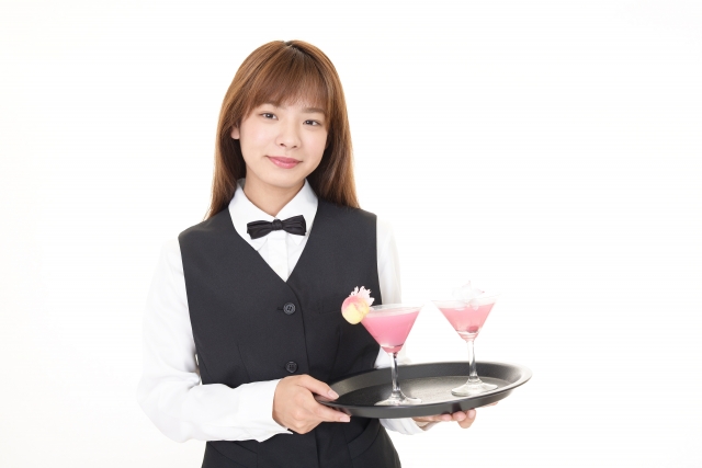 トレーに乗った2つのカクテルを運ぶ女性スタッフ