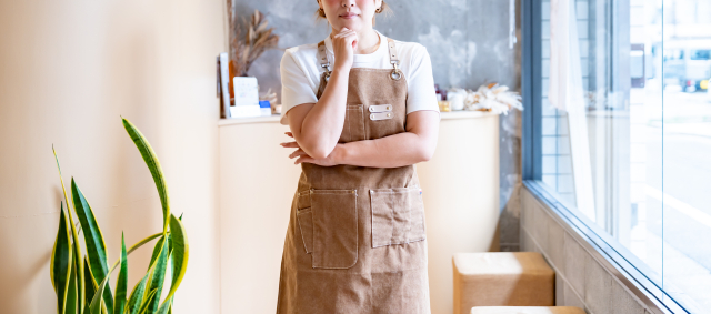 顎に手を当てるカフェスタッフの女性