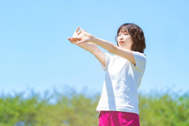 自然の中で目を閉じながら腕を伸ばす半袖の女性