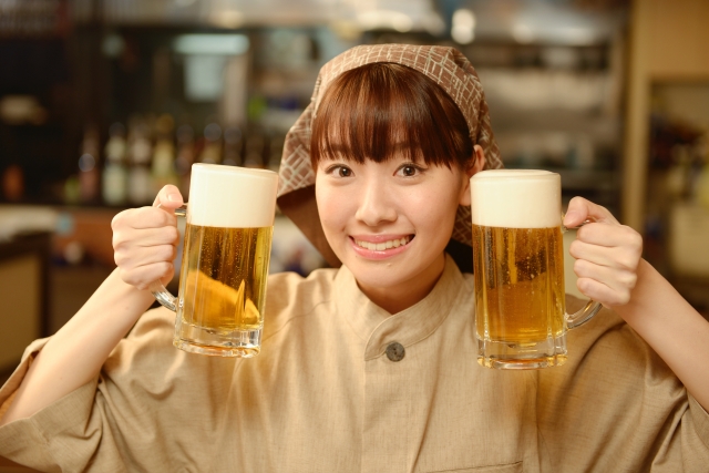 両手に生ビールを持ちこちらに笑顔を向ける飲食店の女性スタッフ