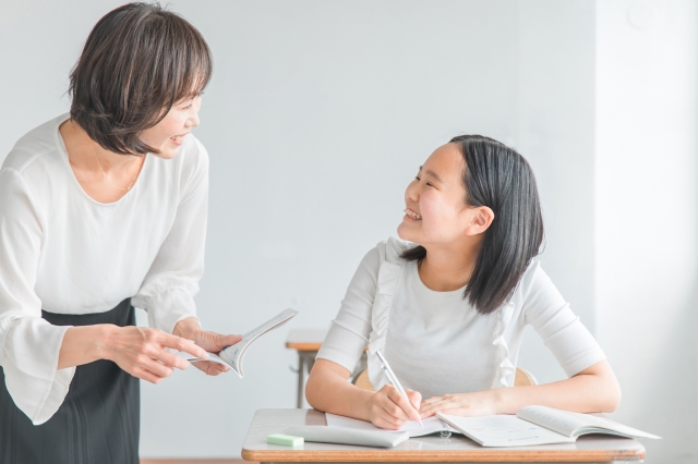 勉強する女子生徒と微笑み合う女性塾講師
