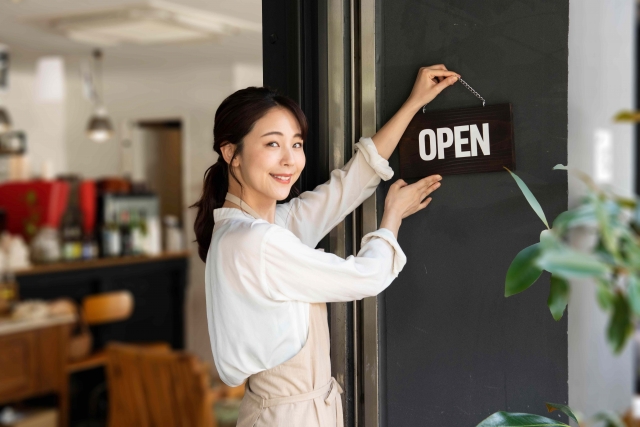 お店の扉の札を「OPEN」にするポニーテールの女性スタッフ