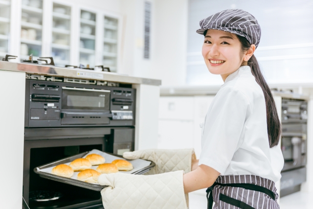 焼きたてのパンを機械から取り出す笑顔の女性スタッフ