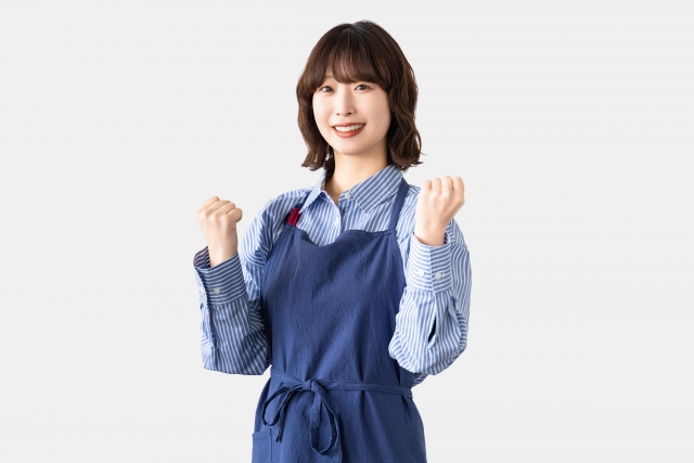 ガッツポーズをしながらこちらに微笑むエプロン姿の女性