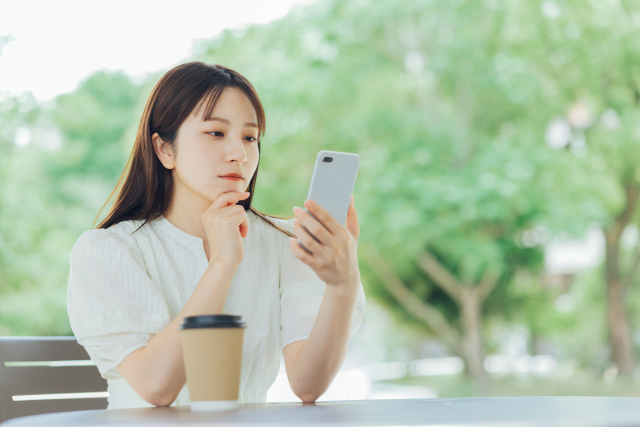 テラス席でスマホを見ながら考え込むブラウス姿の女性