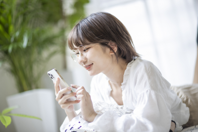 ソファに座ってスマホを見つめるメガネをかけた女性
