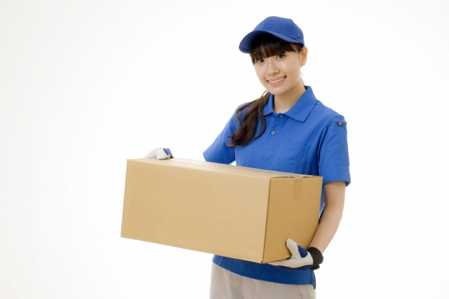 段ボール箱を抱えてこちらに微笑む引っ越し業者の女性スタッフ