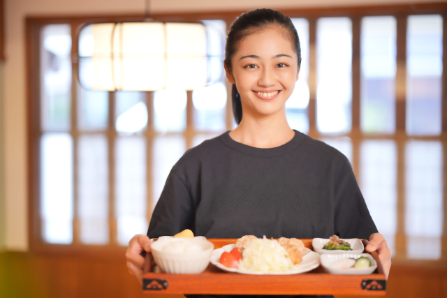定食を持つ笑顔の居酒屋店員の女性