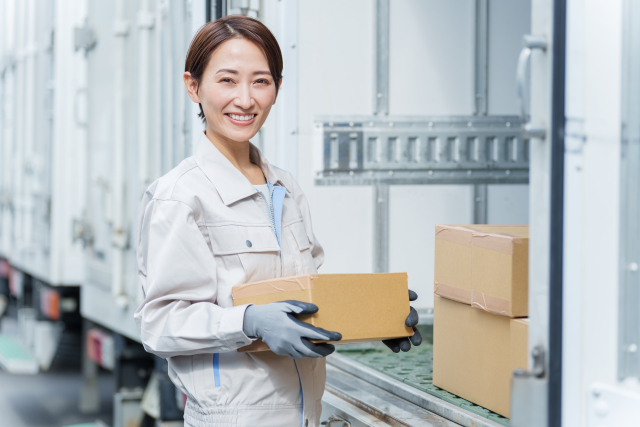 小さめの段ボールを運ぶ作業服姿の女性