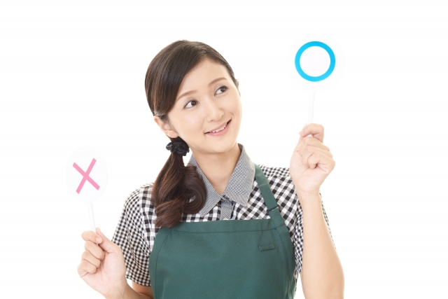 エプロンをしてマルとバツの札を上げる女性