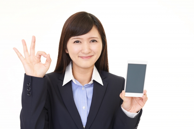 笑顔でスマホを掲げ、OKマークを見せる女性