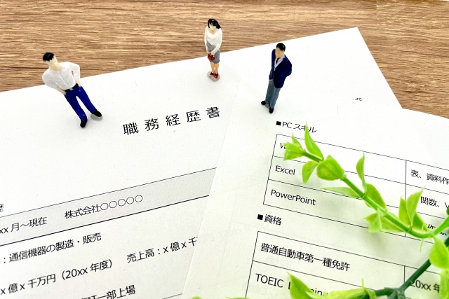 職務経歴書をのぞき込むスーツのミニチュア