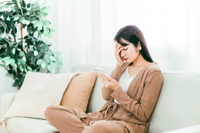 スマホを見つめ頭を抑える部屋着の女性