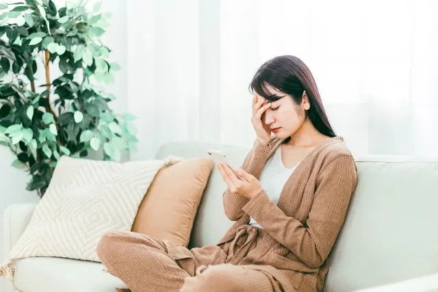 スマホを見つめ頭を抑える部屋着の女性