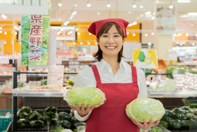 両手にキャベツを持ってこちらに微笑む女性店員