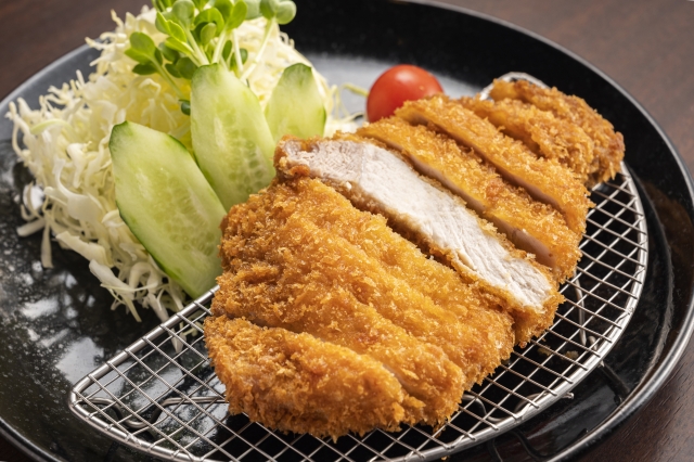 千切りキャベツやミニトマトと一緒に盛り付けられたとんかつのイメージ
