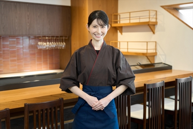 カウンター前で手を前に組みこちらに微笑む女性店員