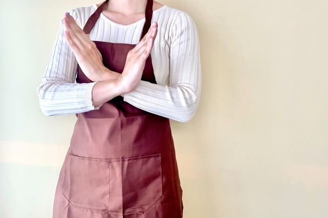腕でバツのマークを作るエプロン姿の女性