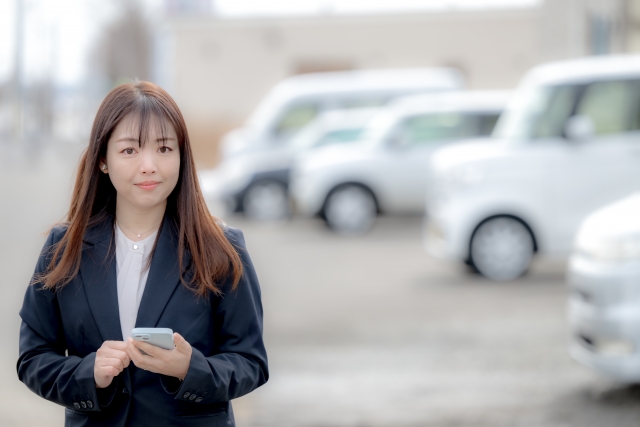 カーショップで車をバックに佇む女性スタッフ