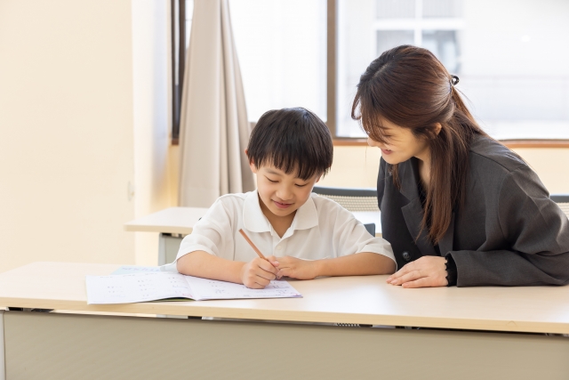 男子児童に一対一で勉強を教える女性講師