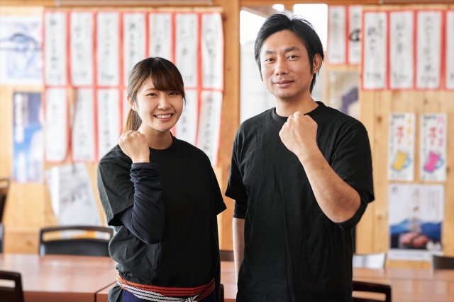 ガッツポーズをしながらこちらに微笑む男女の飲食店スタッフ