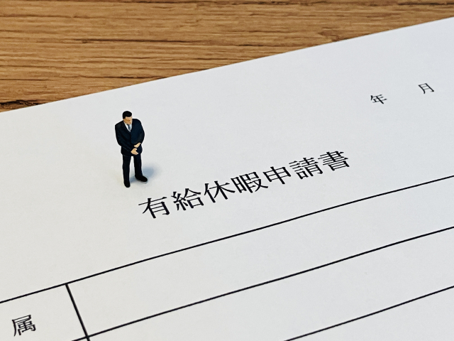 有給休暇申請書と、その上に乗せられたスーツのミニチュア