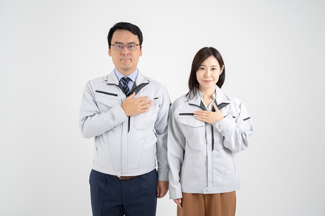 胸に手を当ててこちらを見つめる作業着を着た男女