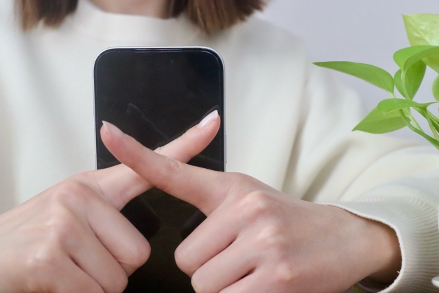 スマートフォンの前で両手の人差し指を重ね、バツのマークを作る女性の手元