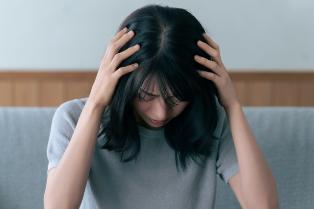 薄暗い部屋で頭を抱えて悩む女性