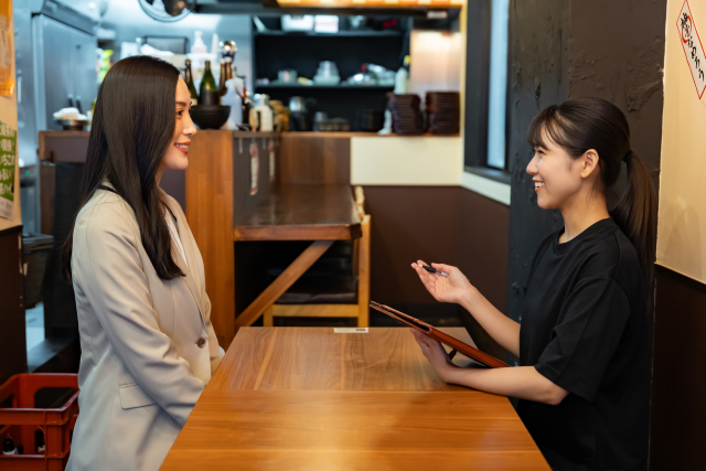 飲食店の面接に訪れた女性と業務や待遇について説明する女性スタッフ