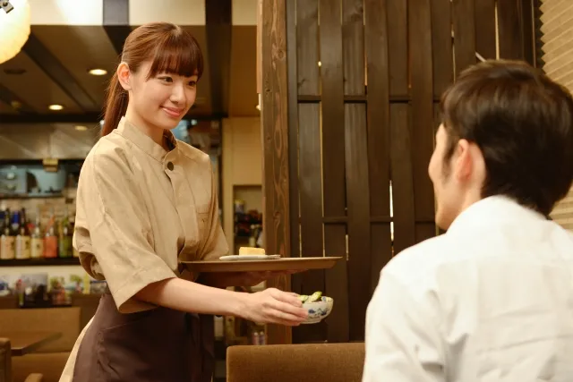 男性客に料理を配膳する飲食店の女性スタッフ