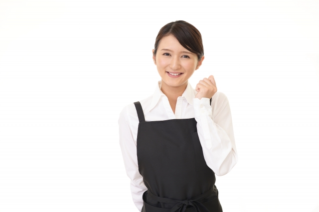 ガッツポーズをしながらこちらに微笑む黒いエプロンを身に付けた女性