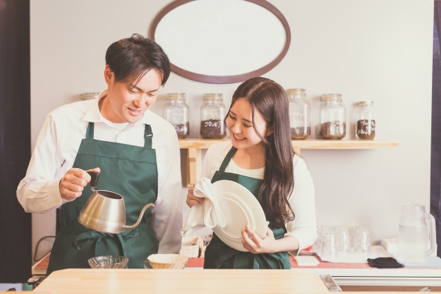コーヒーを淹れている男性カフェスタッフと、見守りながら皿を拭く女性スタッフ