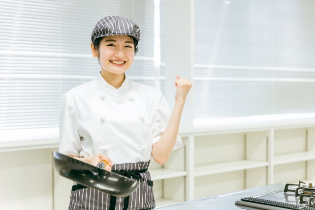 片手にフライパンを持ちながらこちらに笑顔でガッツポーズをする女性スタッフ